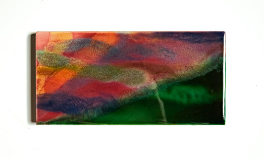 This image features a glazed ceramic artwork titled "Sunrise," measuring 3x6 inches. The artwork depicts an abstract landscape in a vibrant blend of red, orange, green, and blue hues, creating a striking visual effect.