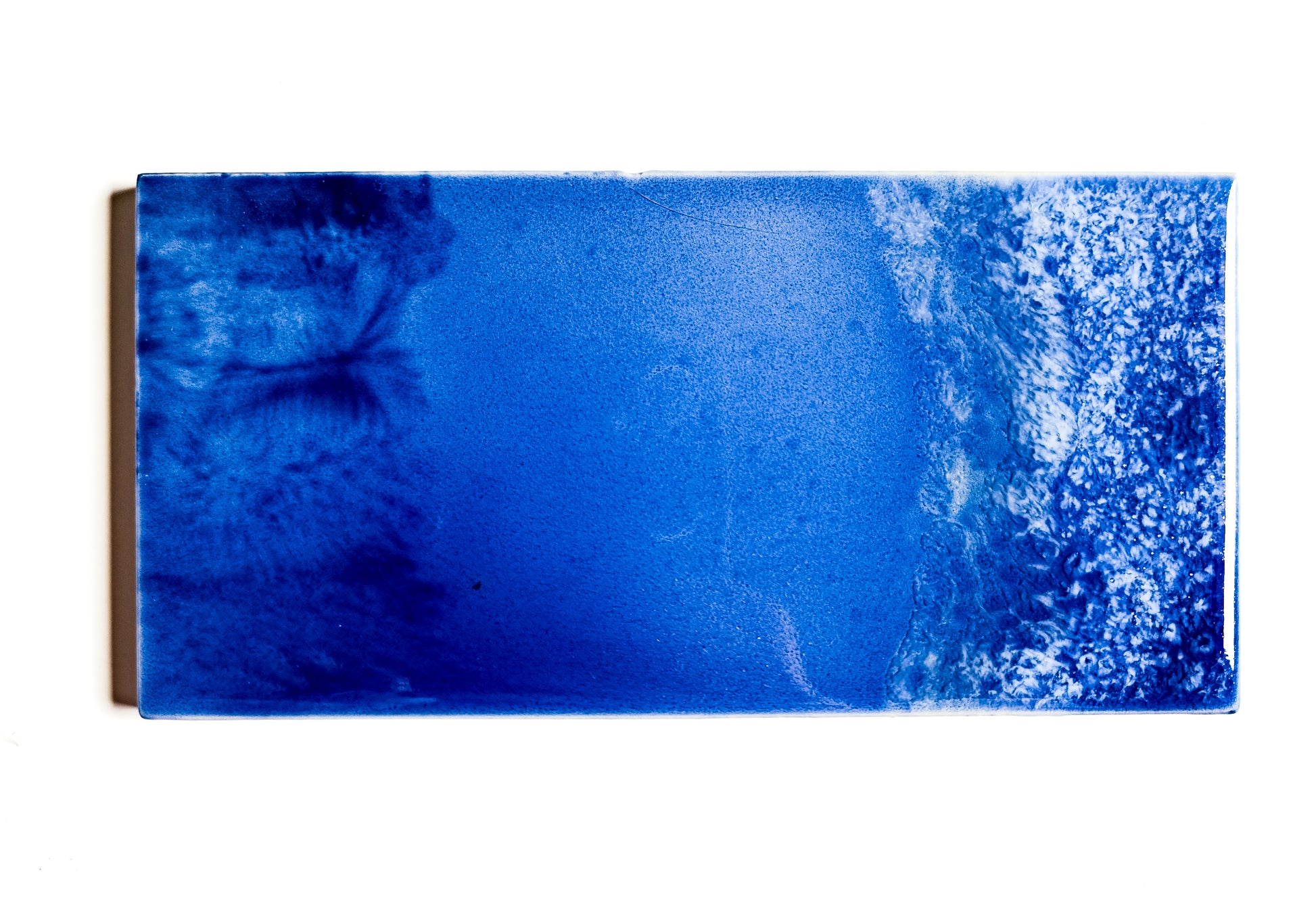 This image features a glazed ceramic tile titled "Waves," crafted by the artist Jackfield. The ceramic piece measures 3x6 inches and showcases an intense blue color with white speckles that create a striking visual effect, reminiscent of ocean waves.
