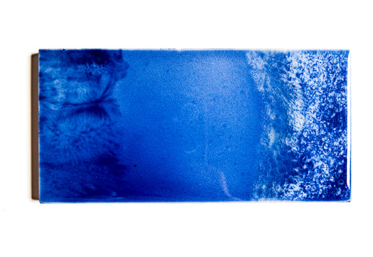 This image features a glazed ceramic tile titled "Waves," crafted by the artist Jackfield. The ceramic piece measures 3x6 inches and showcases an intense blue color with white speckles that create a striking visual effect, reminiscent of ocean waves.